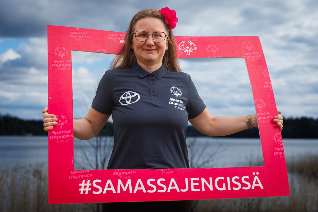Laura Laukkanen poseeraamassa iloisena kameralle punaisen #SamassaJengissä -kehyksen sisällä ulkona.